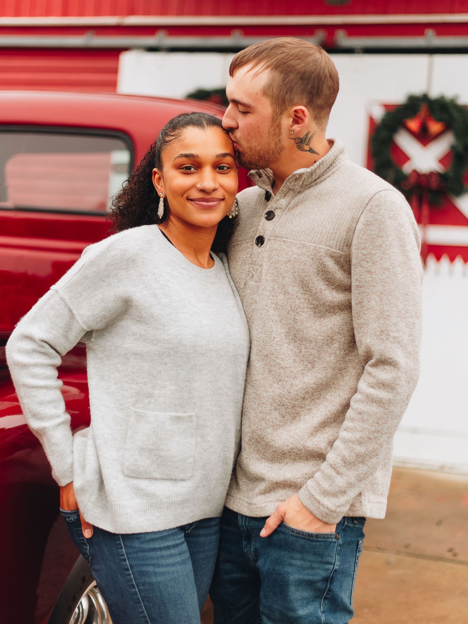 Couple wearing matching grey sweaters posing against a bright red wall.