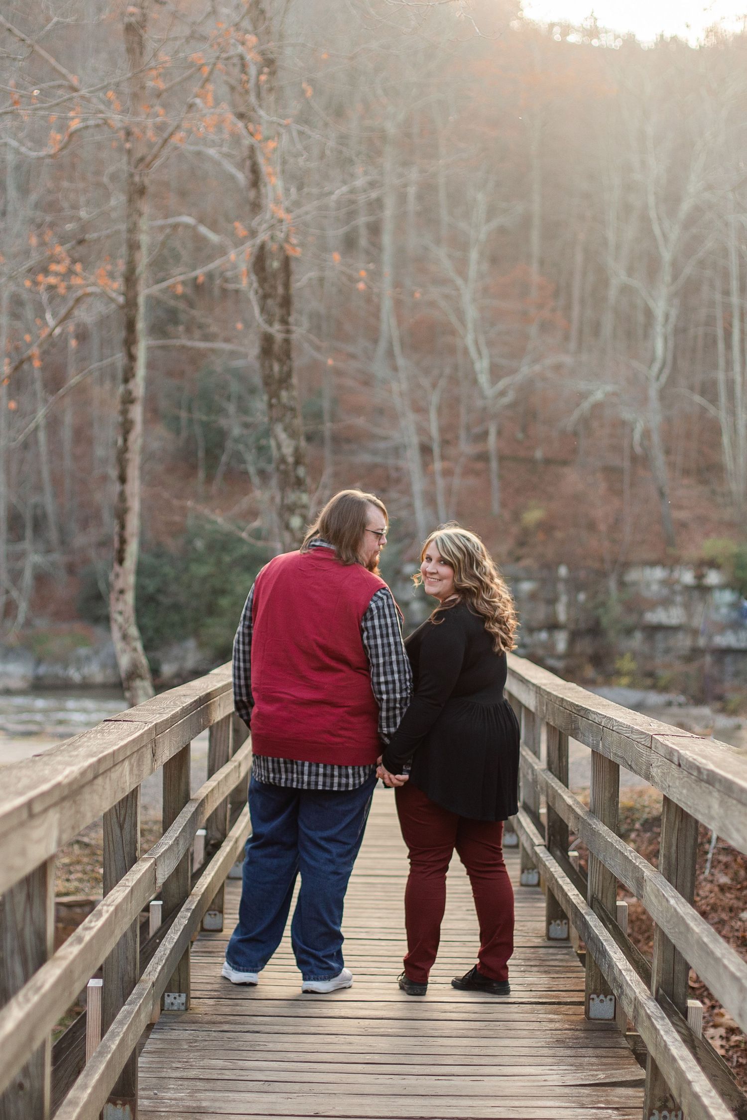 A couple shares an intimate moment on a wooden bridge during sunset surrounded by autumn trees.