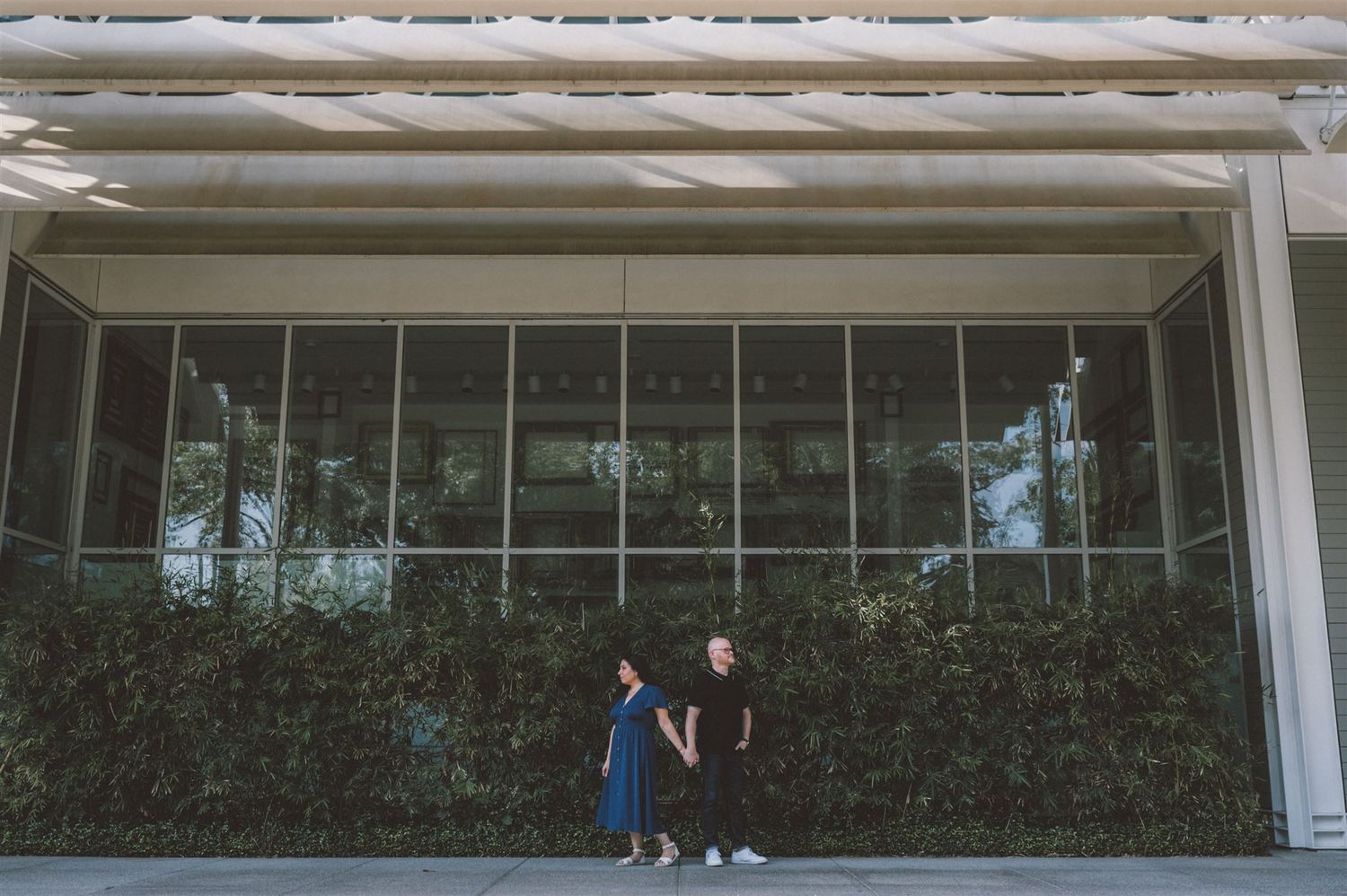 Couple poses in front of modern glass building with green wall.