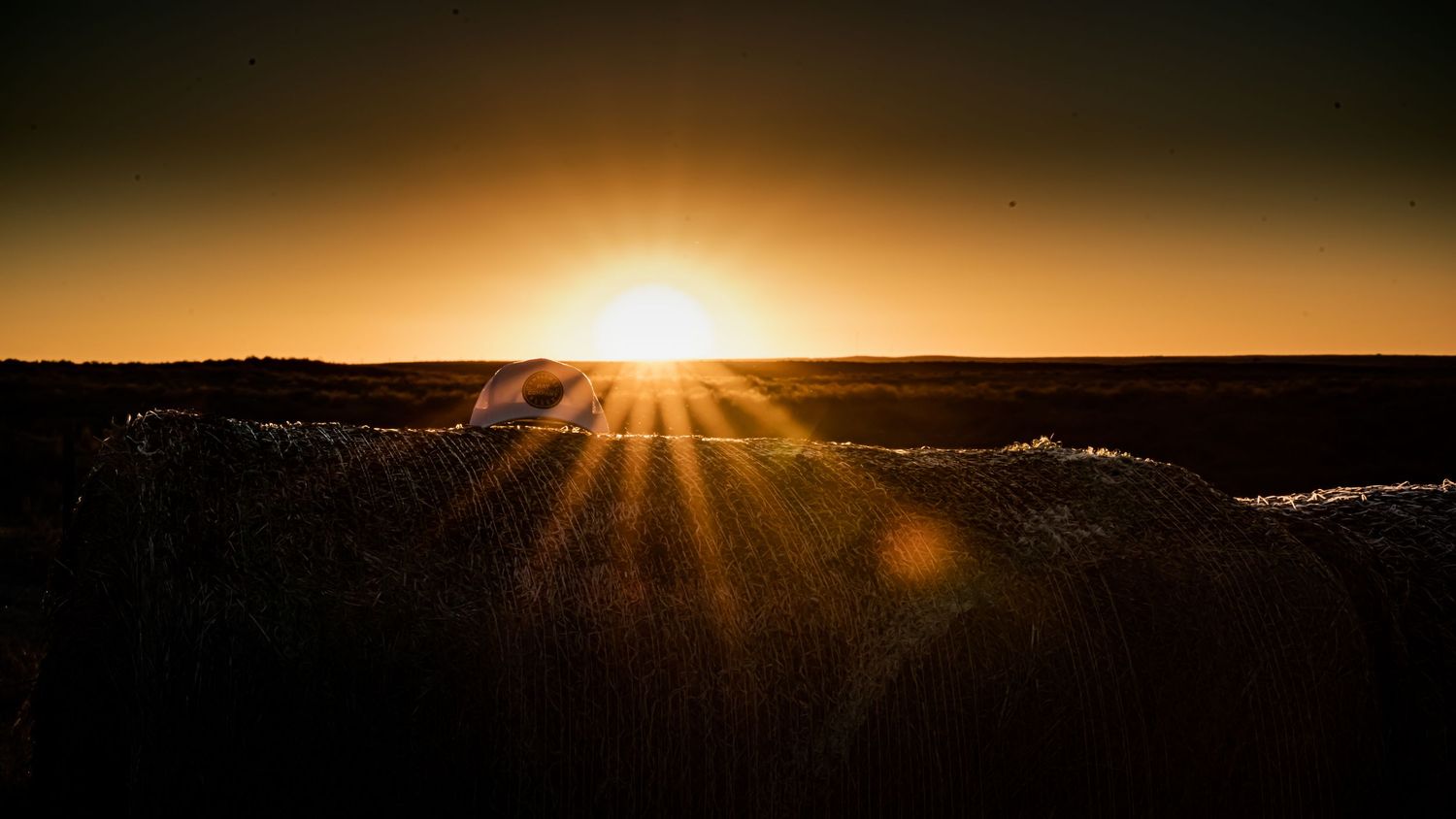 Dramatic orange sunset with sun rays bursting over dark horizon silhouetting the landscape.