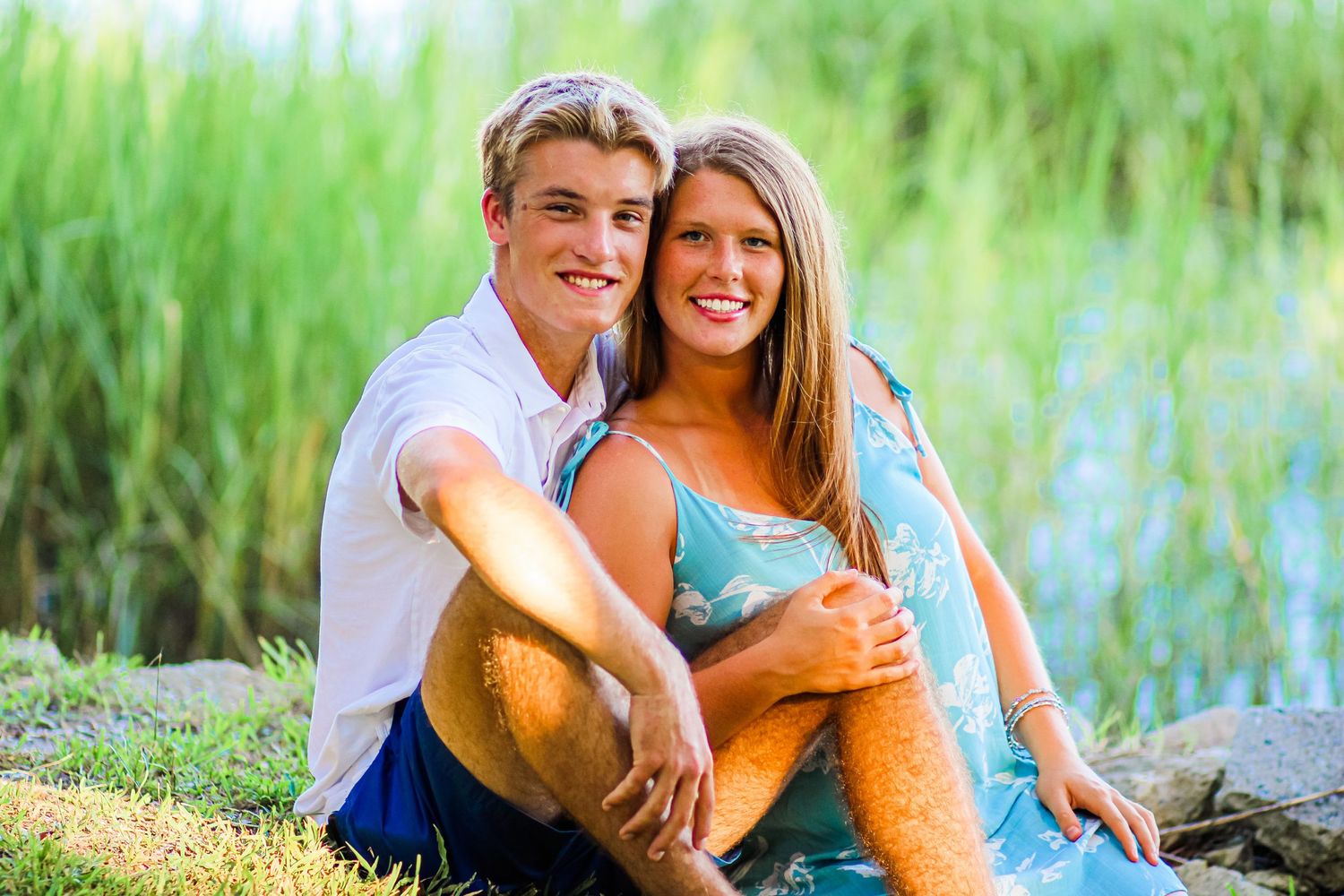 Happy couple sits together by waterfront on sunny afternoon.