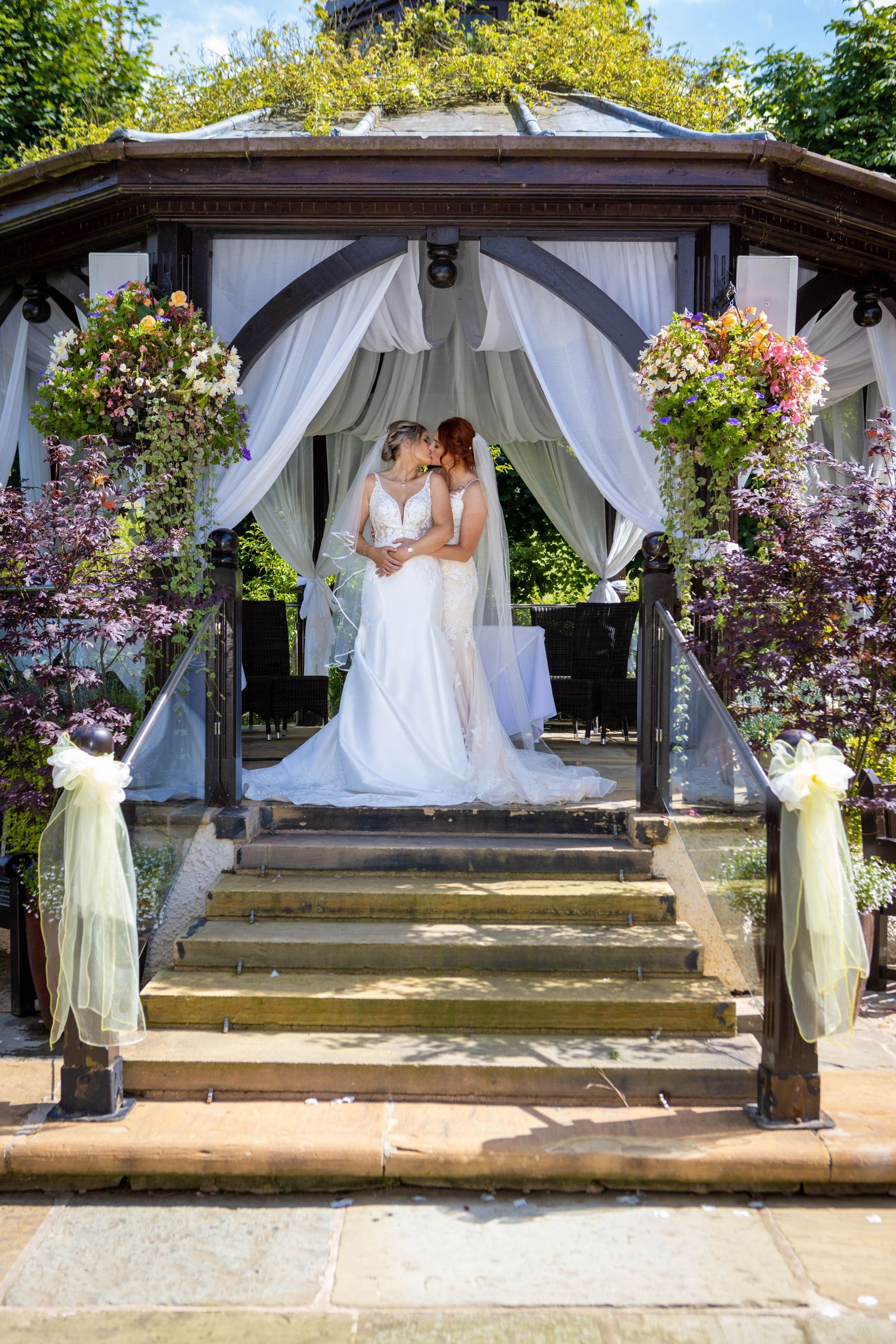 Elegant white gazebo decorated with flowing fabric and flowers serves as a romantic outdoor wedding ceremony venue.