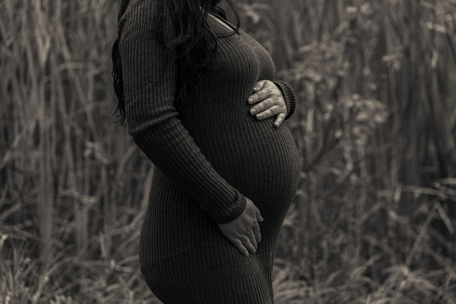 Black and white maternity silhouette showing pregnant belly in ribbed dress.