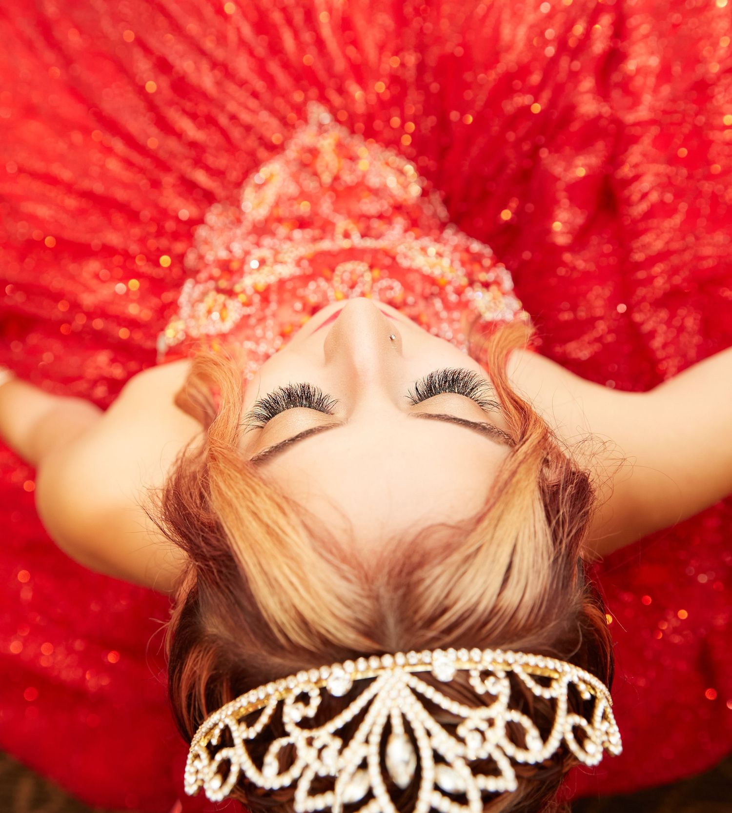 Overhead view of someone lying on red fabric with closed eyes and ornate dress details.