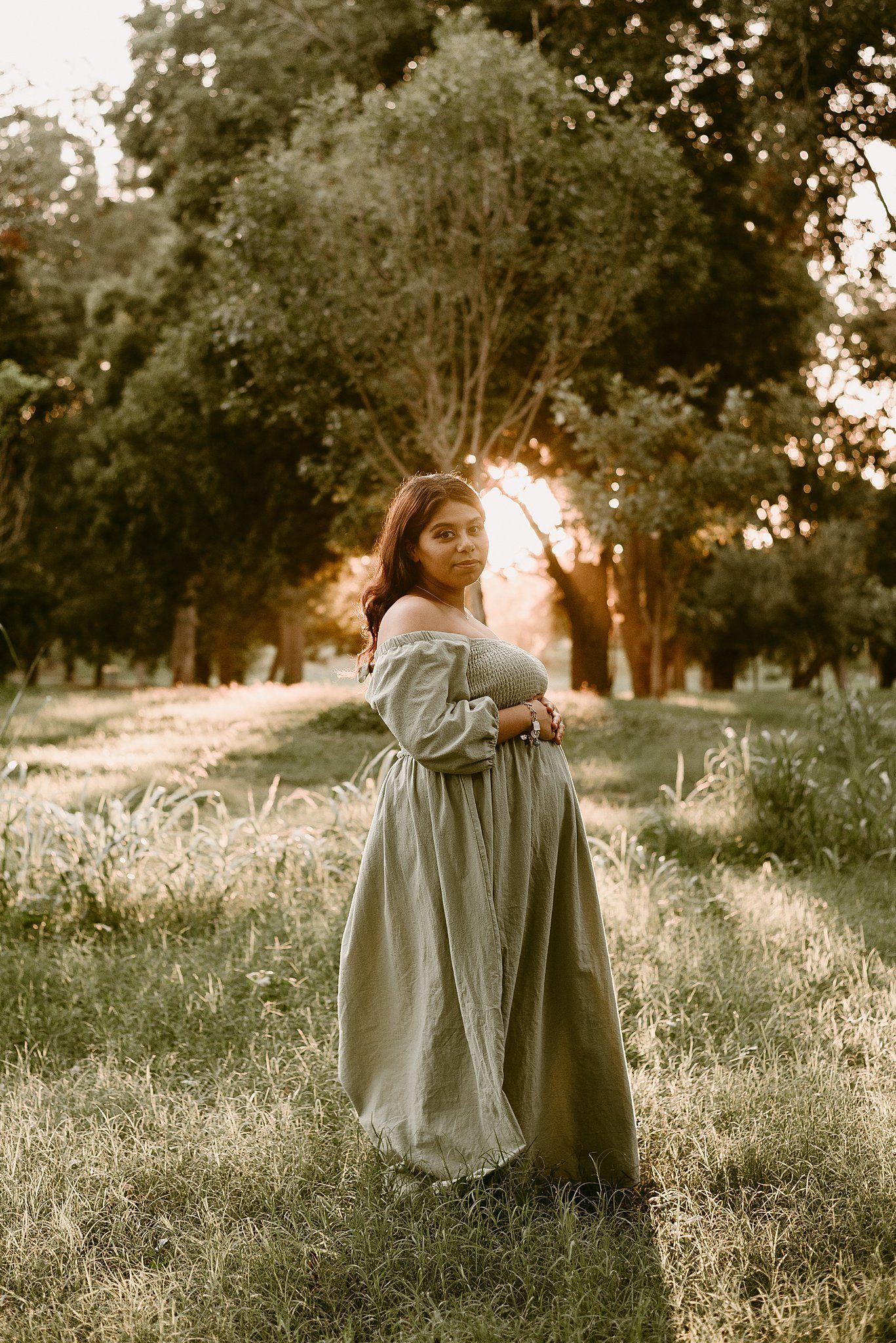 Maternity portrait at sunset with a person in a flowing dress standing in golden light.