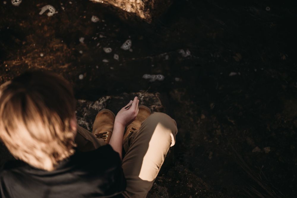 Top-down view of a young person exploring rocks in a dark wooded area.