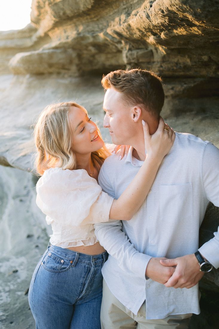 A tender moment between a couple against rocky coastal cliffs during golden hour.