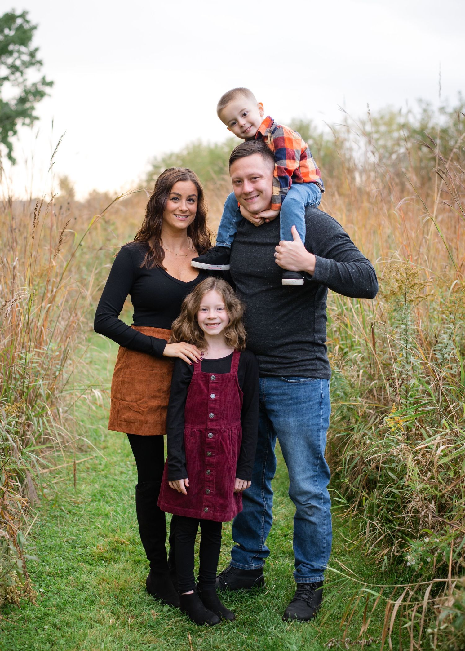 Family of four poses together in a field of tall grass during autumn.