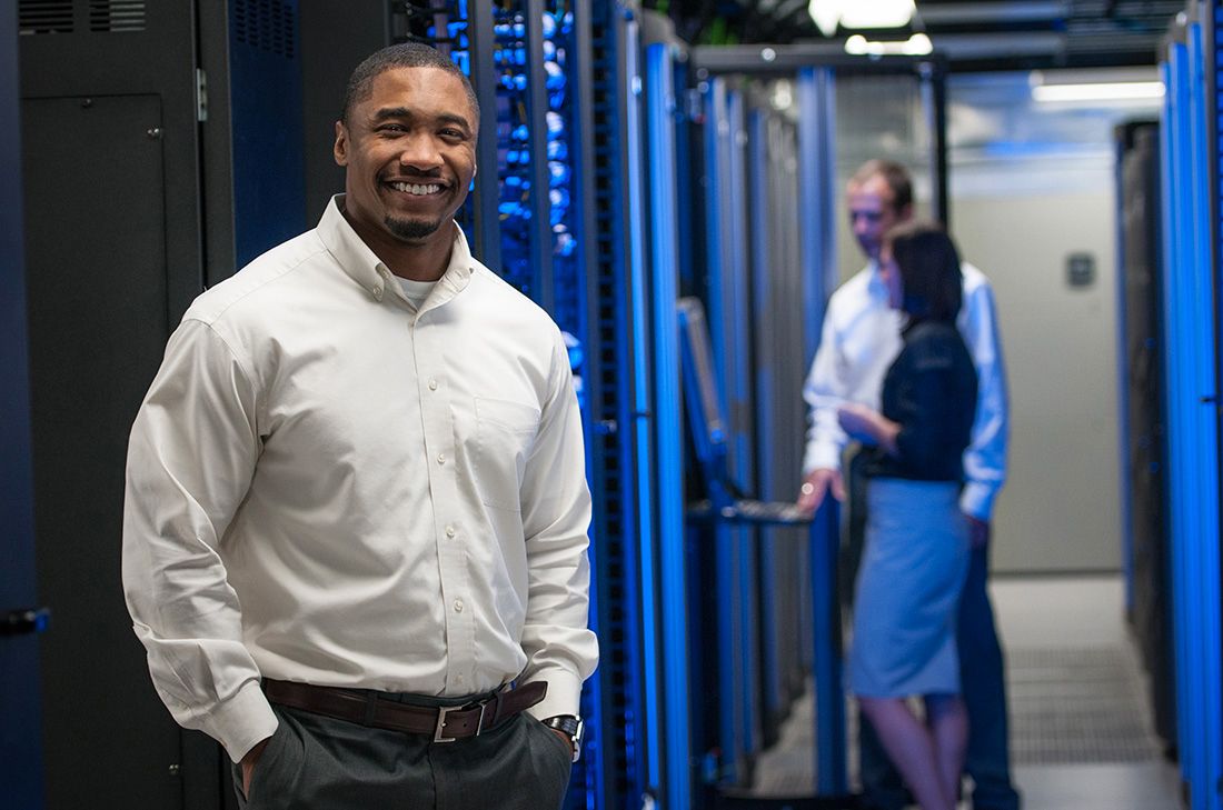 African American portrait in data center with employees in background