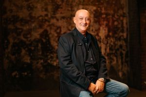 Professional speaker seated against textured backdrop in dramatic lighting.