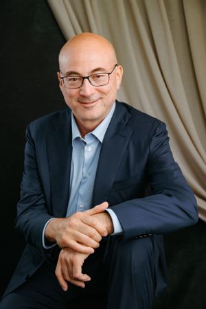 Professional portrait of someone in a navy suit and glasses against a light background.