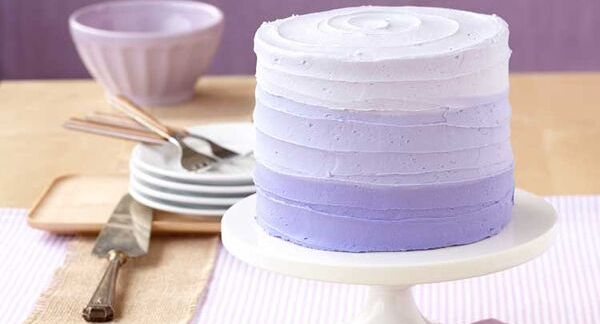 Purple ombre layered cake with textured frosting on white cake stand.