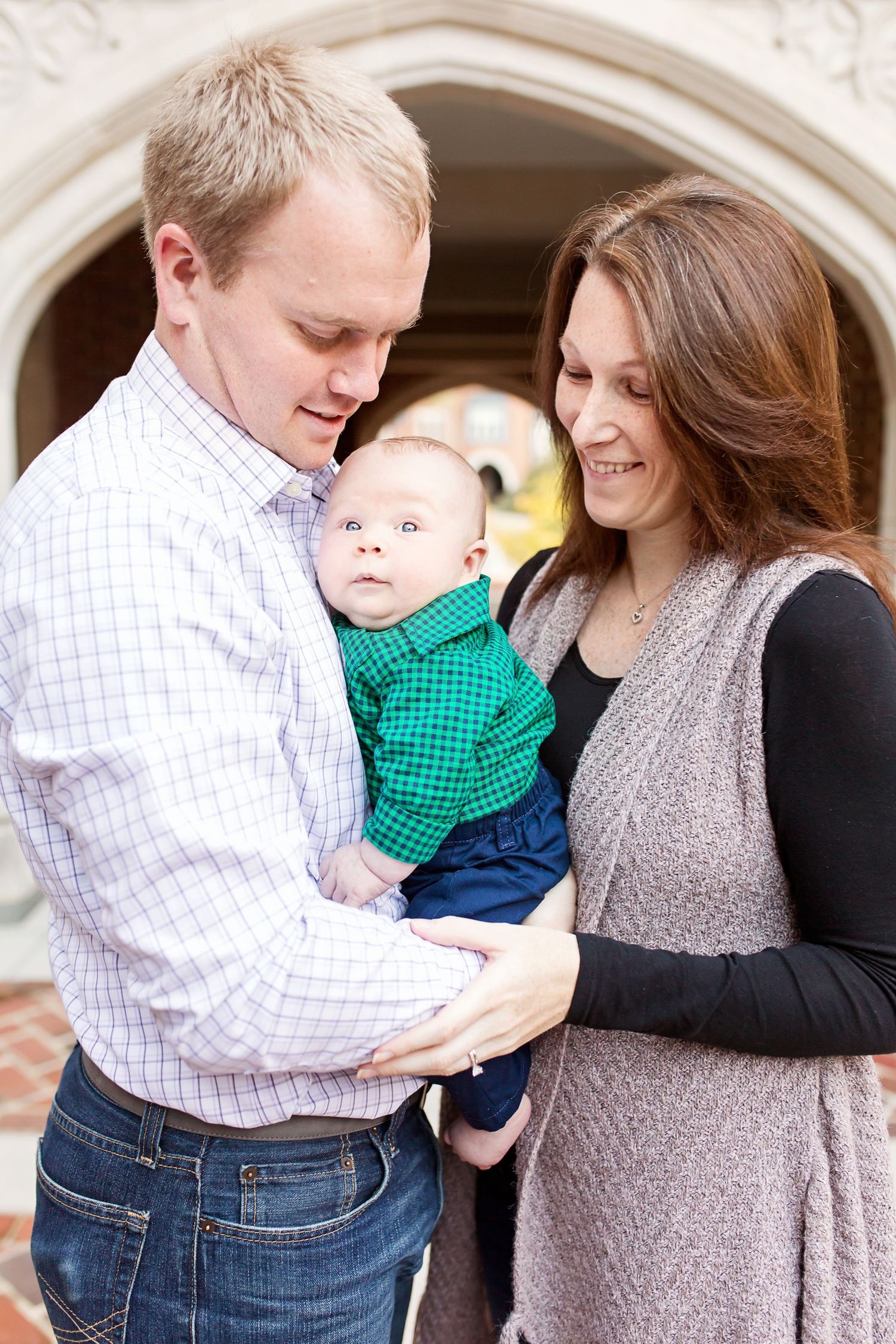 Tender family moment captured under stone archway with baby in green shirt.