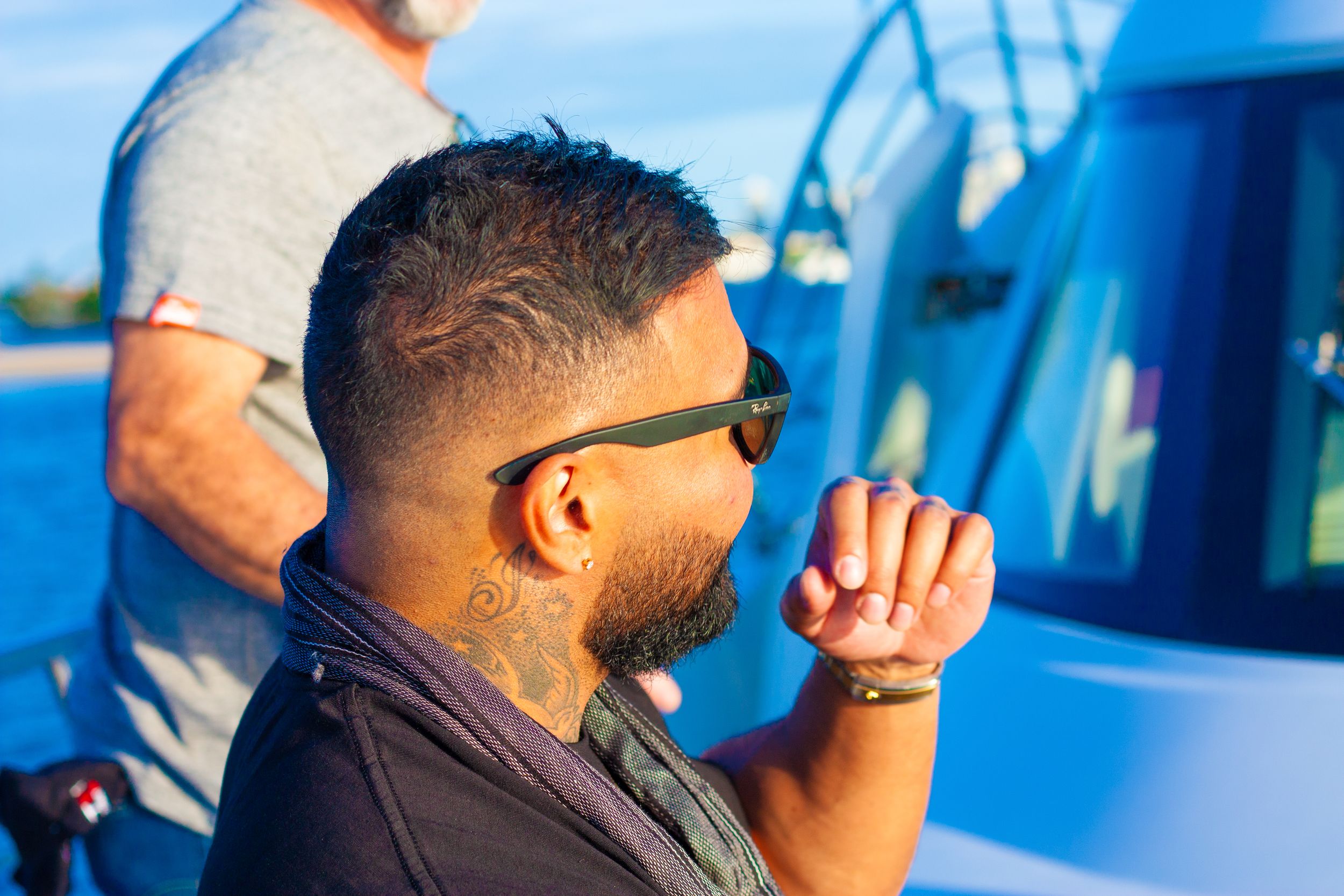 Profile view of someone in sunglasses against blue sky and boat background.