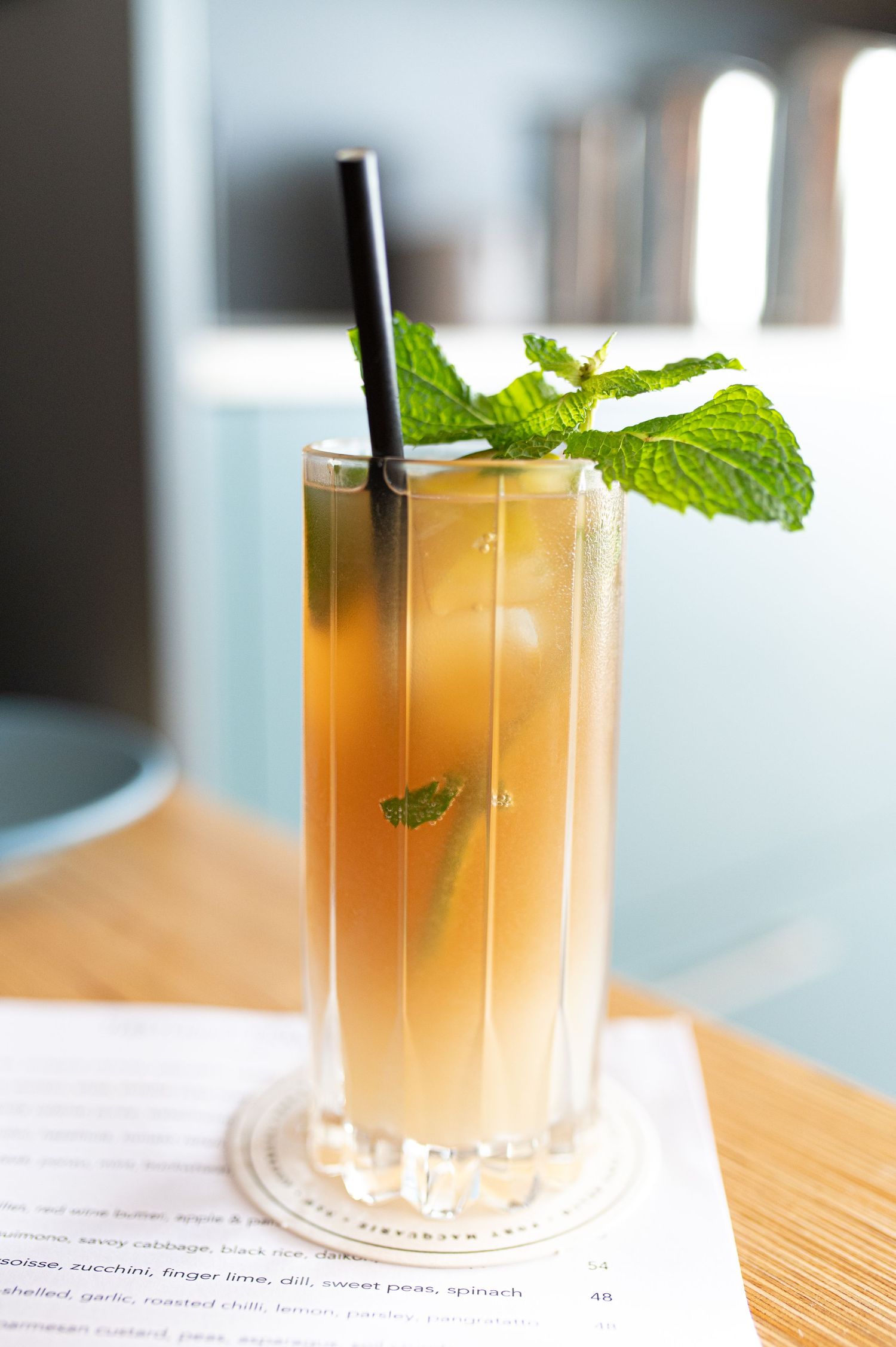 Golden cocktail garnished with fresh mint leaves in a tall glass with black straw.