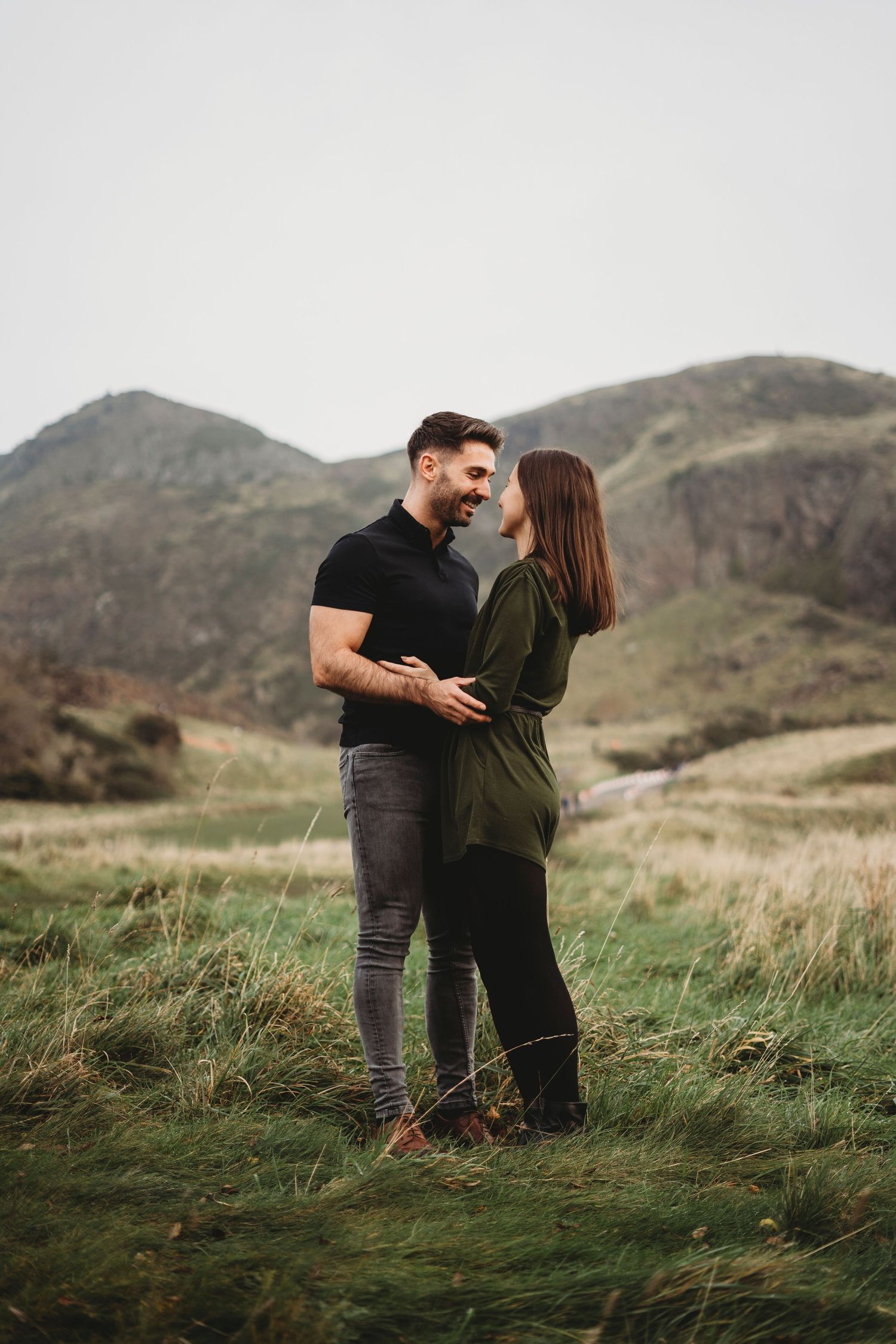 A couple embraces on a hilltop with mountains in the background during golden hour.