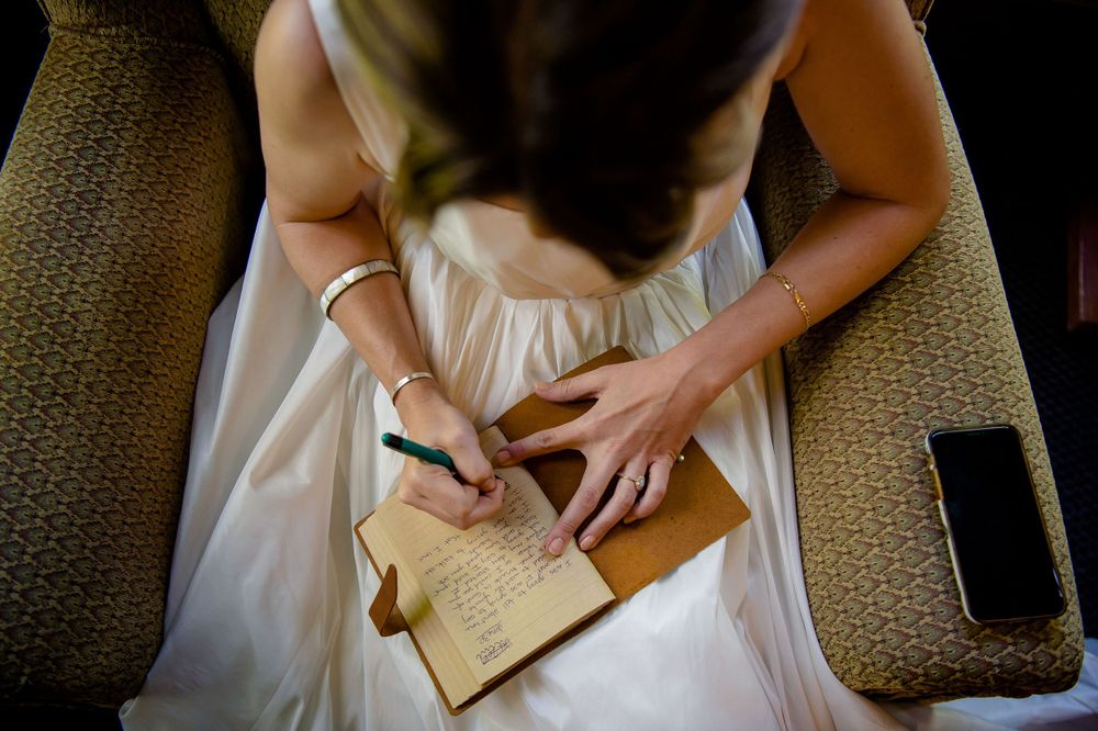 Overhead view of someone in a white dress writing in a journal or notebook on a textured surface.