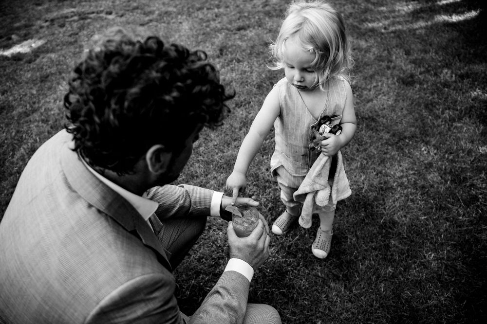 A black and white photograph of a heartwarming moment between an adult and small child in a dress on grass.