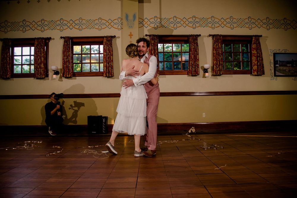 A couple dances together in an empty hall with decorative windows.