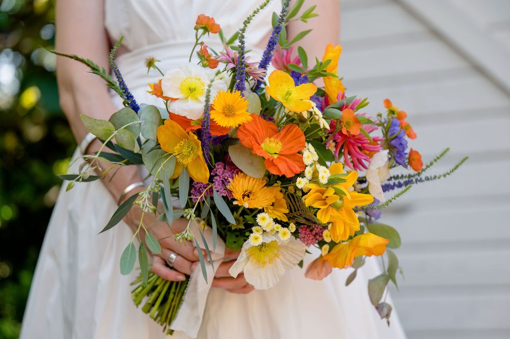 Vibrant wedding bouquet featuring orange, yellow, and purple wildflowers with natural greenery.