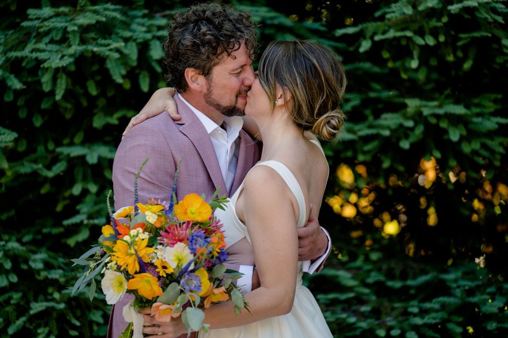 Intimate wedding moment captured with colorful floral bouquet against lush green background.