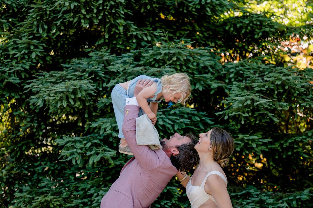 Joyful outdoor family moment with child being lifted up during wedding celebrations.