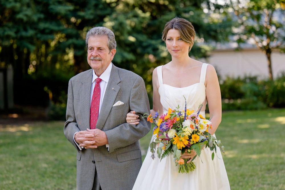 Outdoor wedding portrait with colorful summer bouquet against garden backdrop.