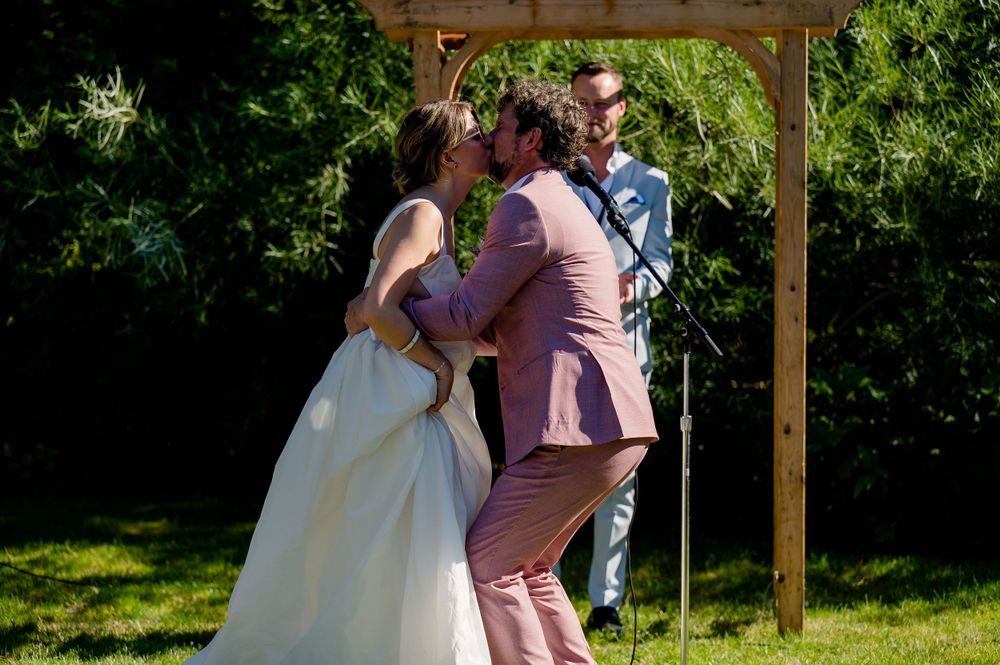 Wedding ceremony moment under wooden arch in sunny garden setting.