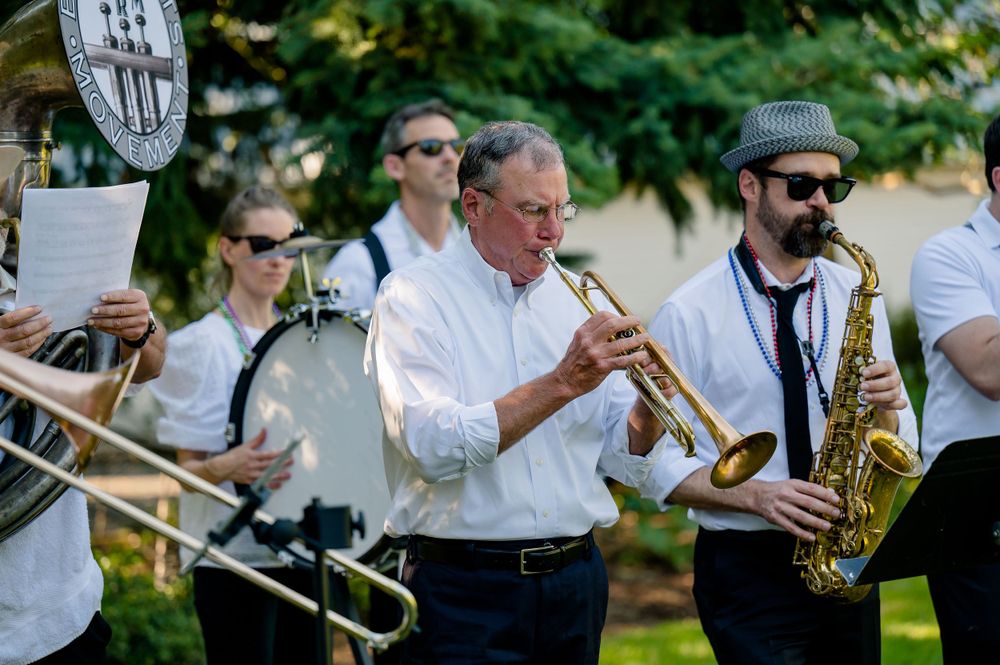A brass band performs outdoors with musicians playing trumpet and saxophone.