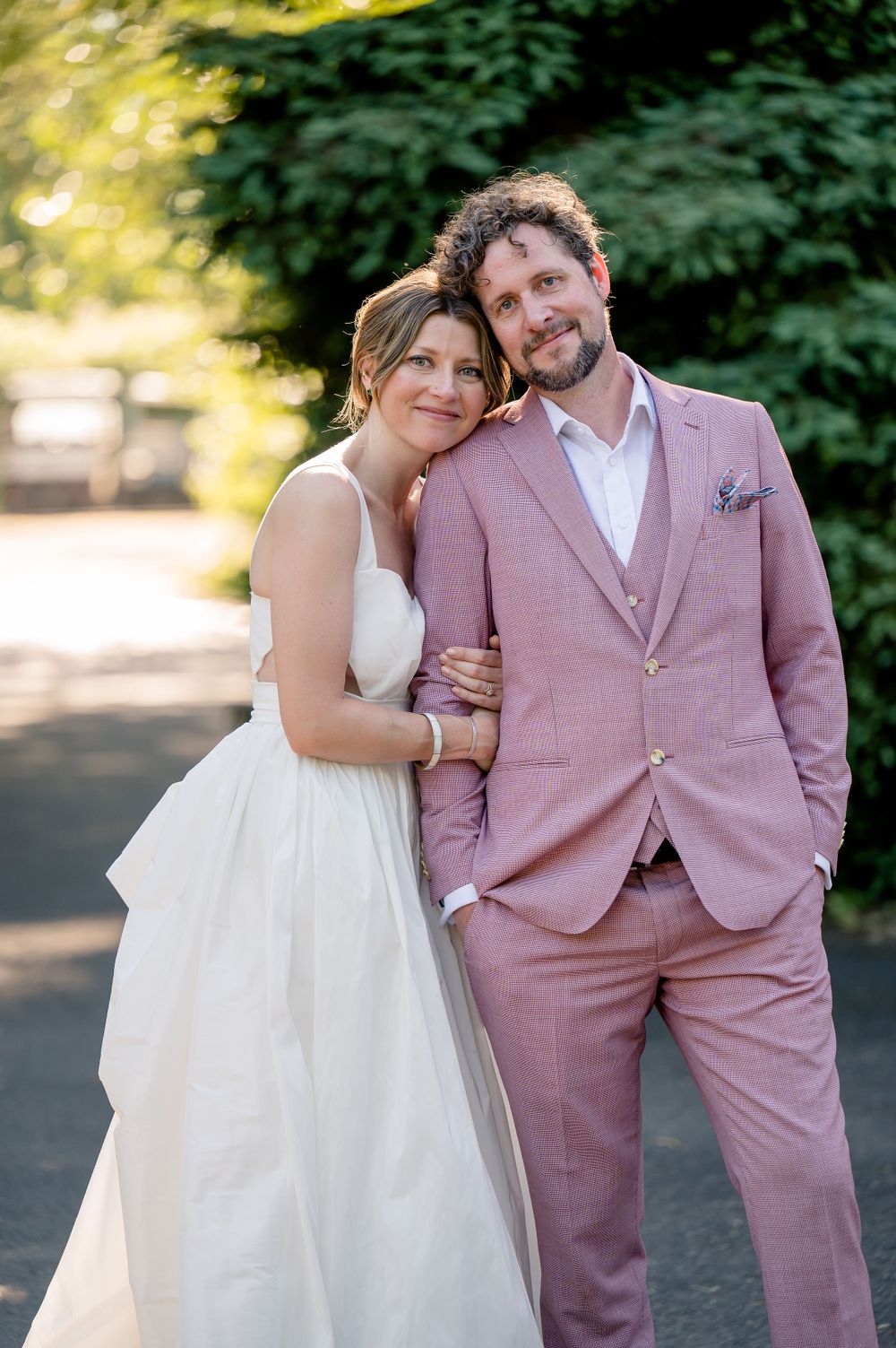Wedding portrait in garden setting with couple in white dress and pink suit.