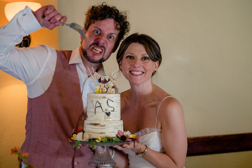 A playful cake cutting moment with a rustic tiered wedding cake.