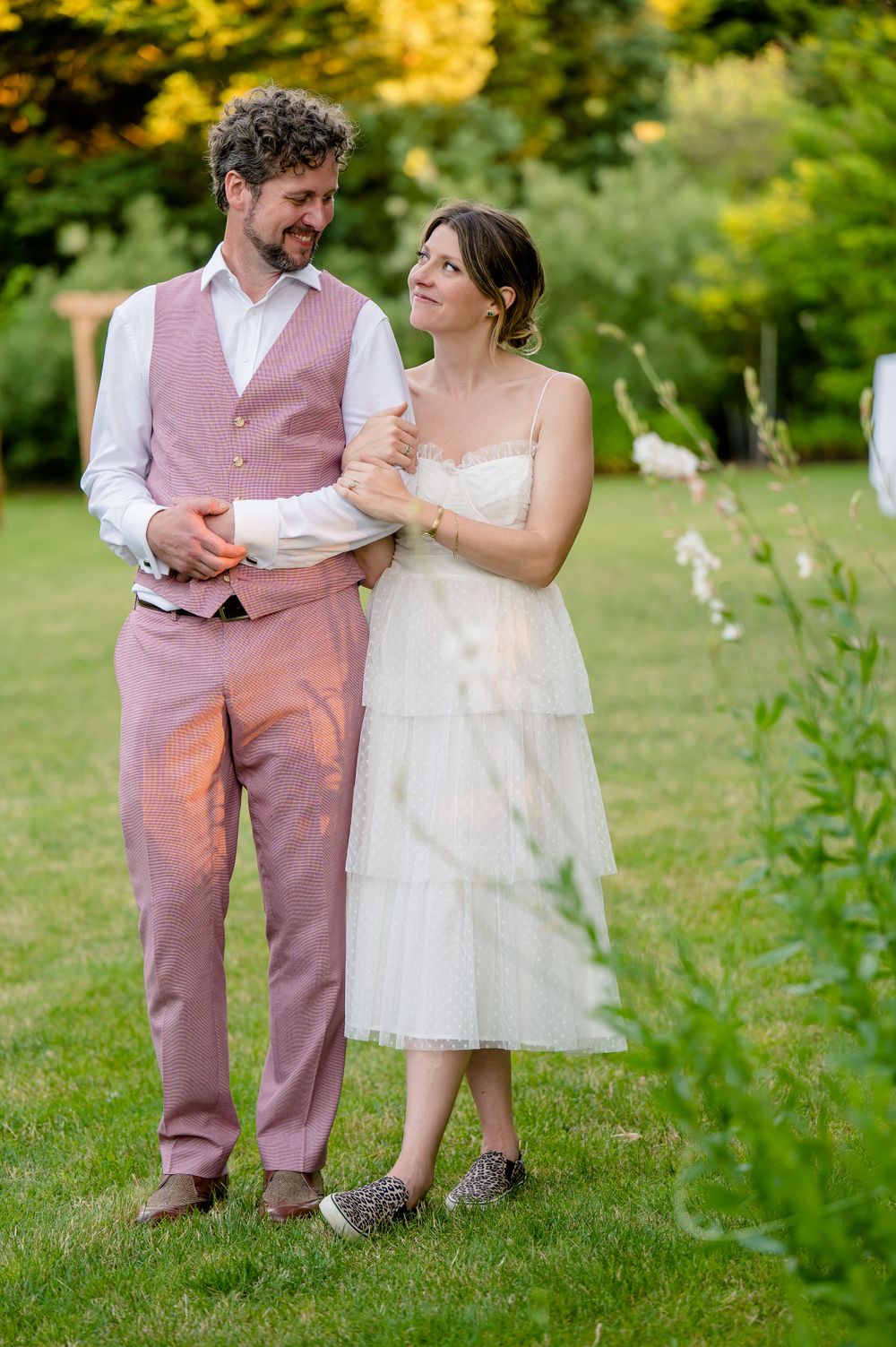 A couple in coordinating pink and white wedding attire stand together in a garden setting.