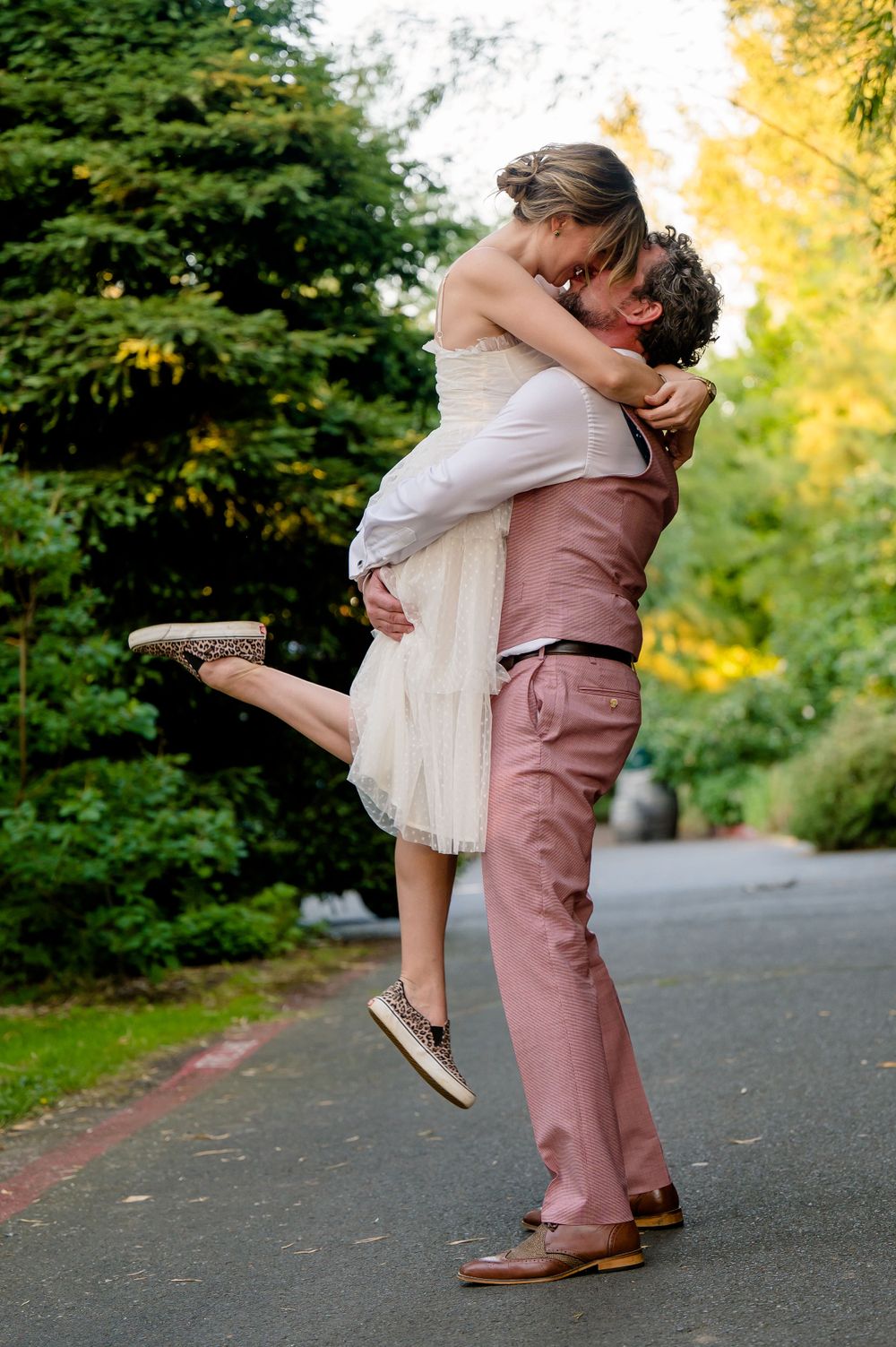 A joyful couple sharing a romantic lift embrace on a tree-lined path.
