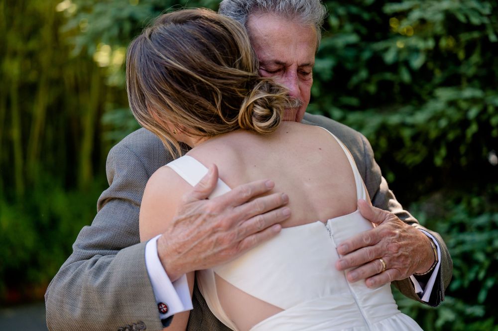 Emotional moment as a father hugs the bride on her wedding day in an outdoor garden setting.