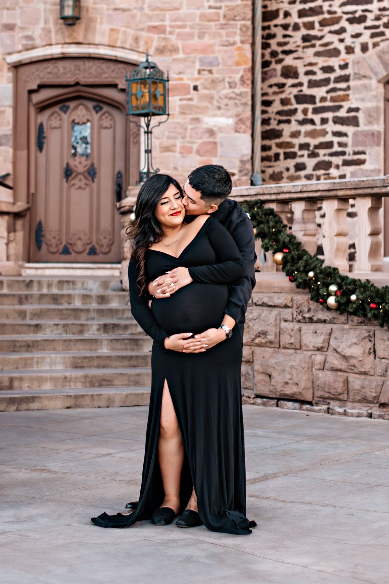 pregnant couple holding one another in front of the highlands ranch mansion staircase
