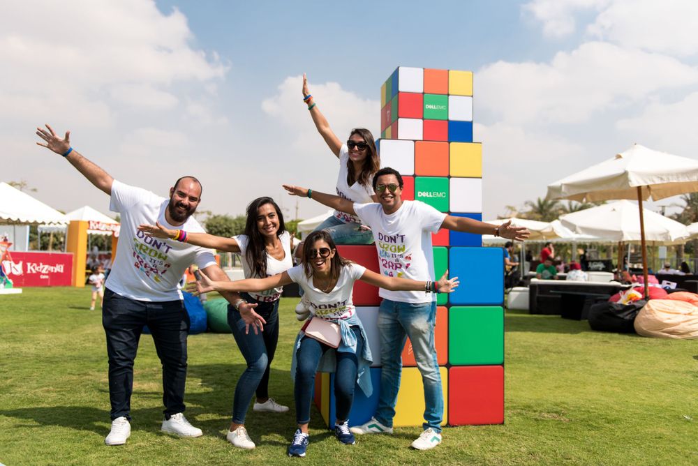 Enthusiastic group poses in front of large colorful building blocks display at outdoor event.