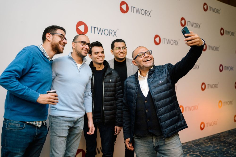 Group of colleagues taking a selfie in front of ITWorx branded backdrop at company event.