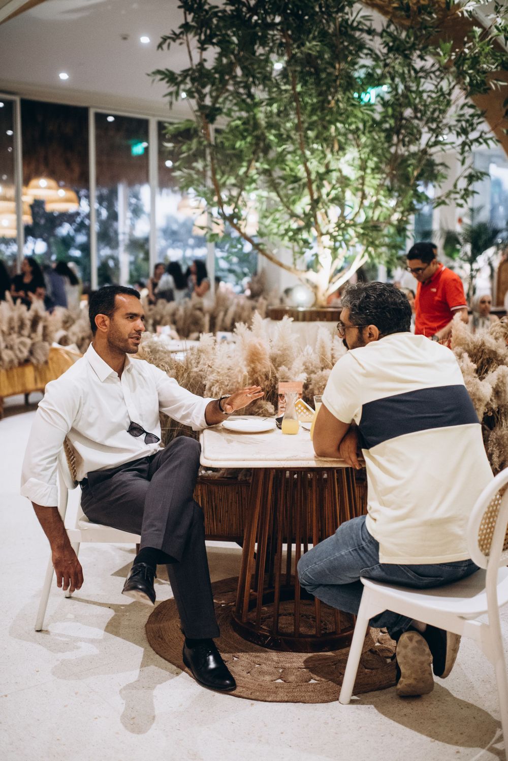 Modern restaurant interior with large decorative tree and diners seated at round tables.