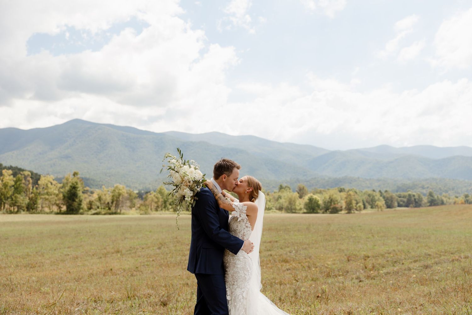 Wedding couple embracing in scenic mountain landscape with dramatic clouds.