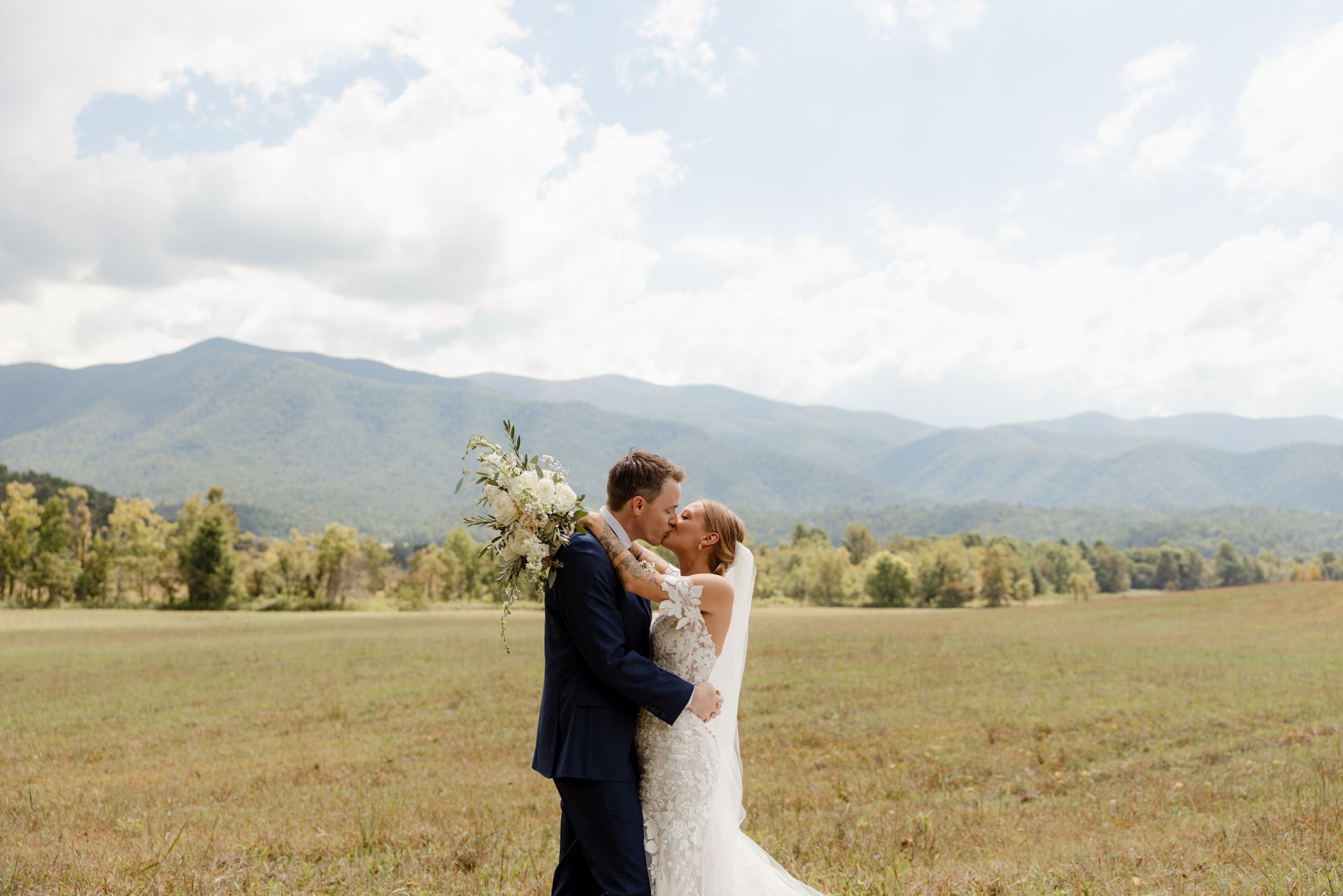 Wedding couple embracing in scenic mountain landscape with dramatic clouds.