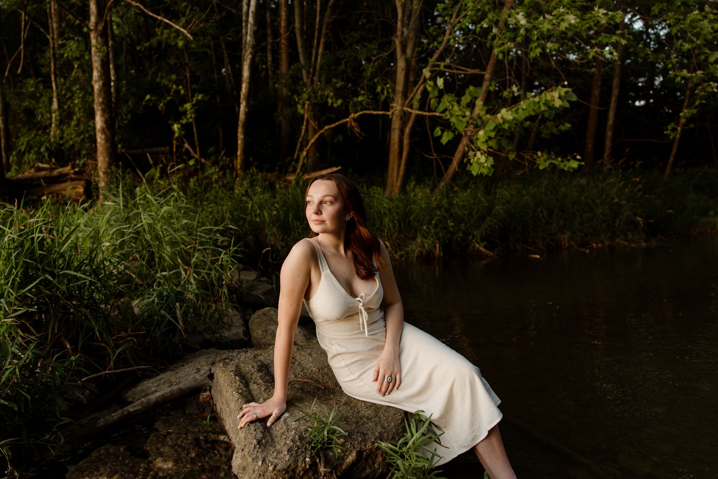 Romantic couple in white outfits posing near a serene lake surrounded by trees.