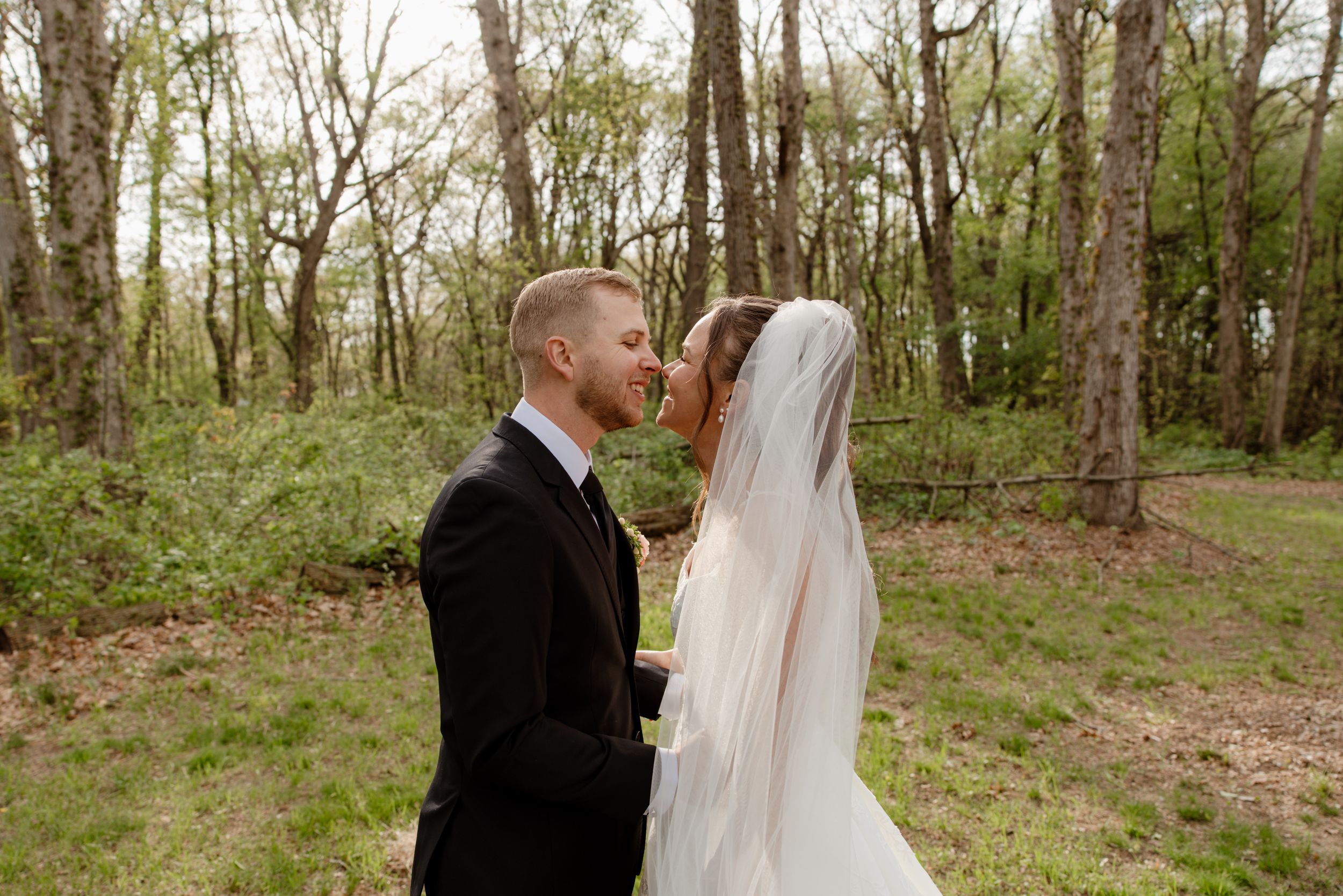A couple shares an intimate kiss in a wooded forest setting during their wedding day.