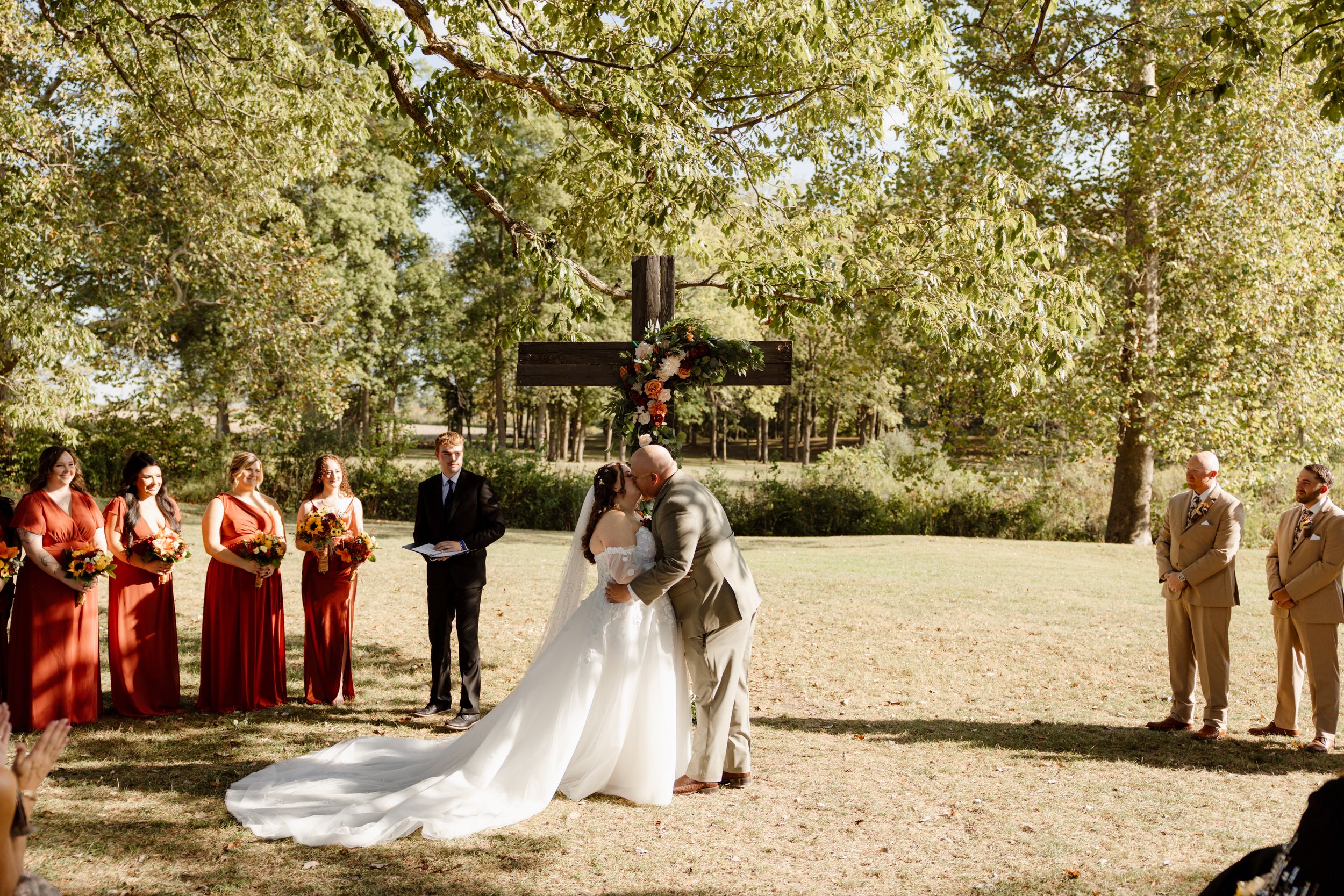 Wedding party gathered under trees during outdoor ceremony with bridesmaids in red dresses.