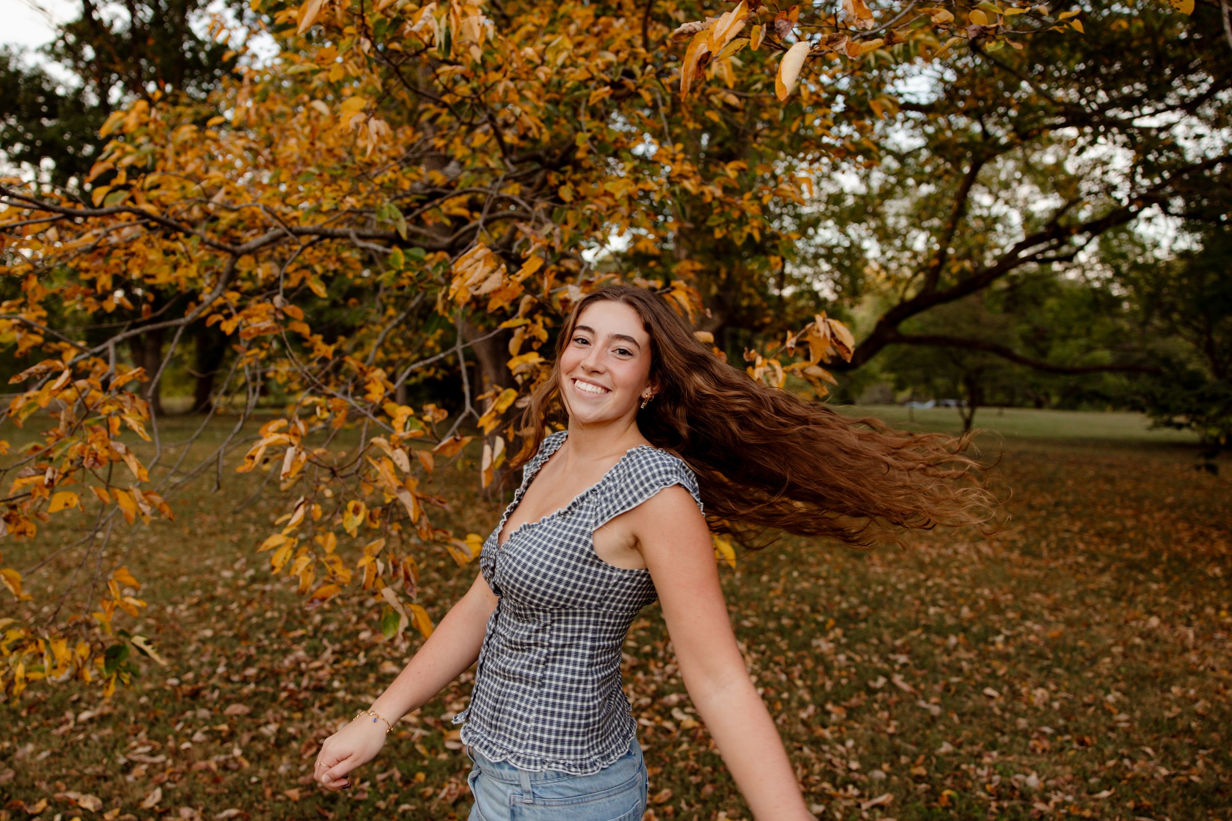 A woman spins joyfully in a park surrounded by autumn leaves and golden sunlight.