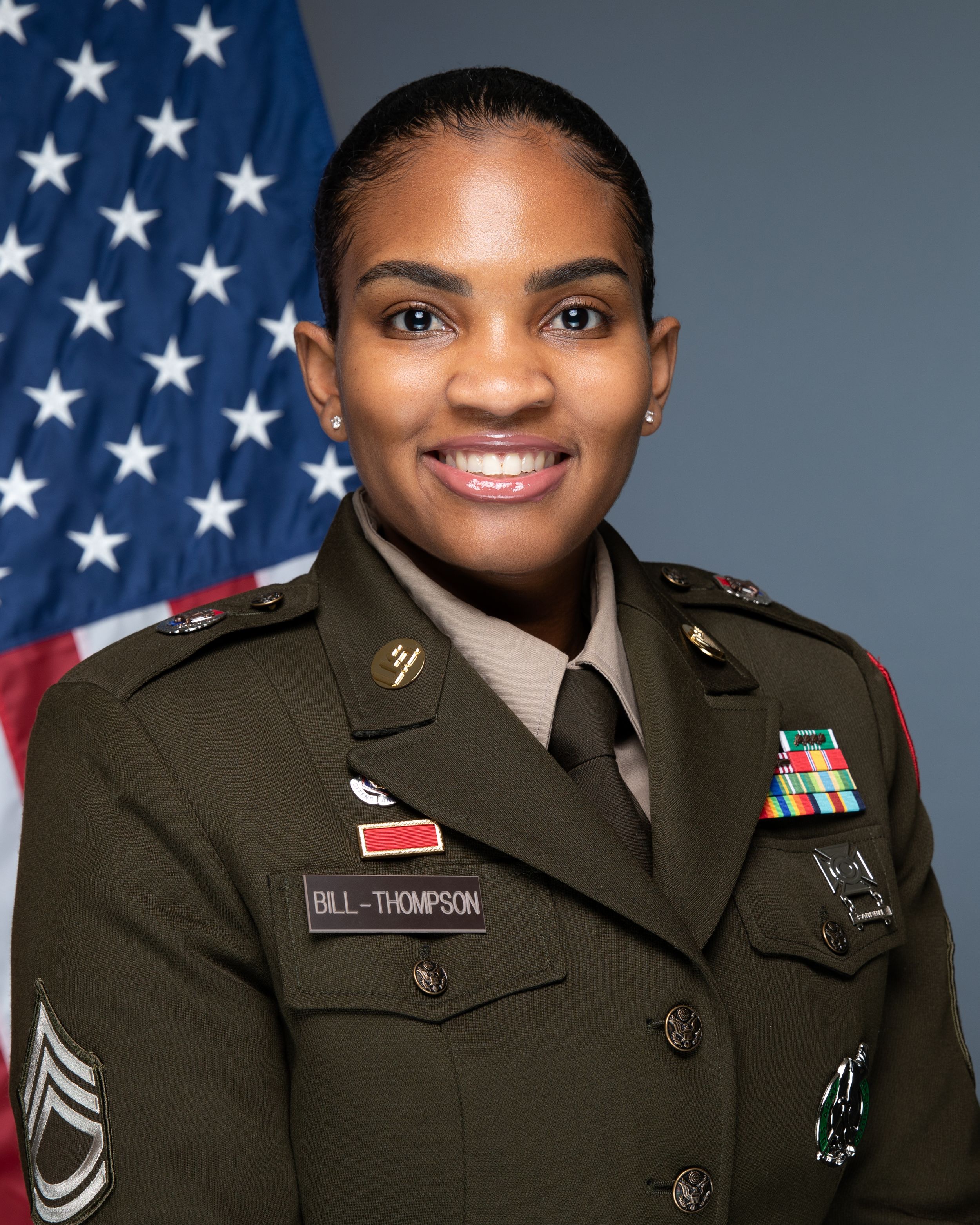 U.S. Army soldier in dress uniform with name tag Bill-Thompson smiling in official military portrait with American flag.
