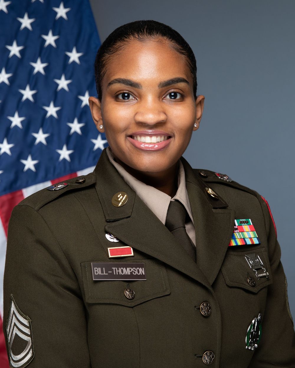 U.S. Army soldier in dress uniform with name tag Bill-Thompson smiling in official military portrait with American flag.