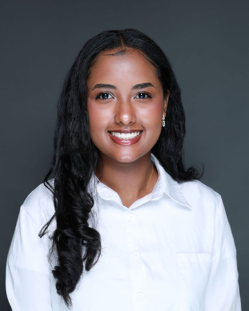 Professional headshot of person in white collared shirt against dark background with bright smile.