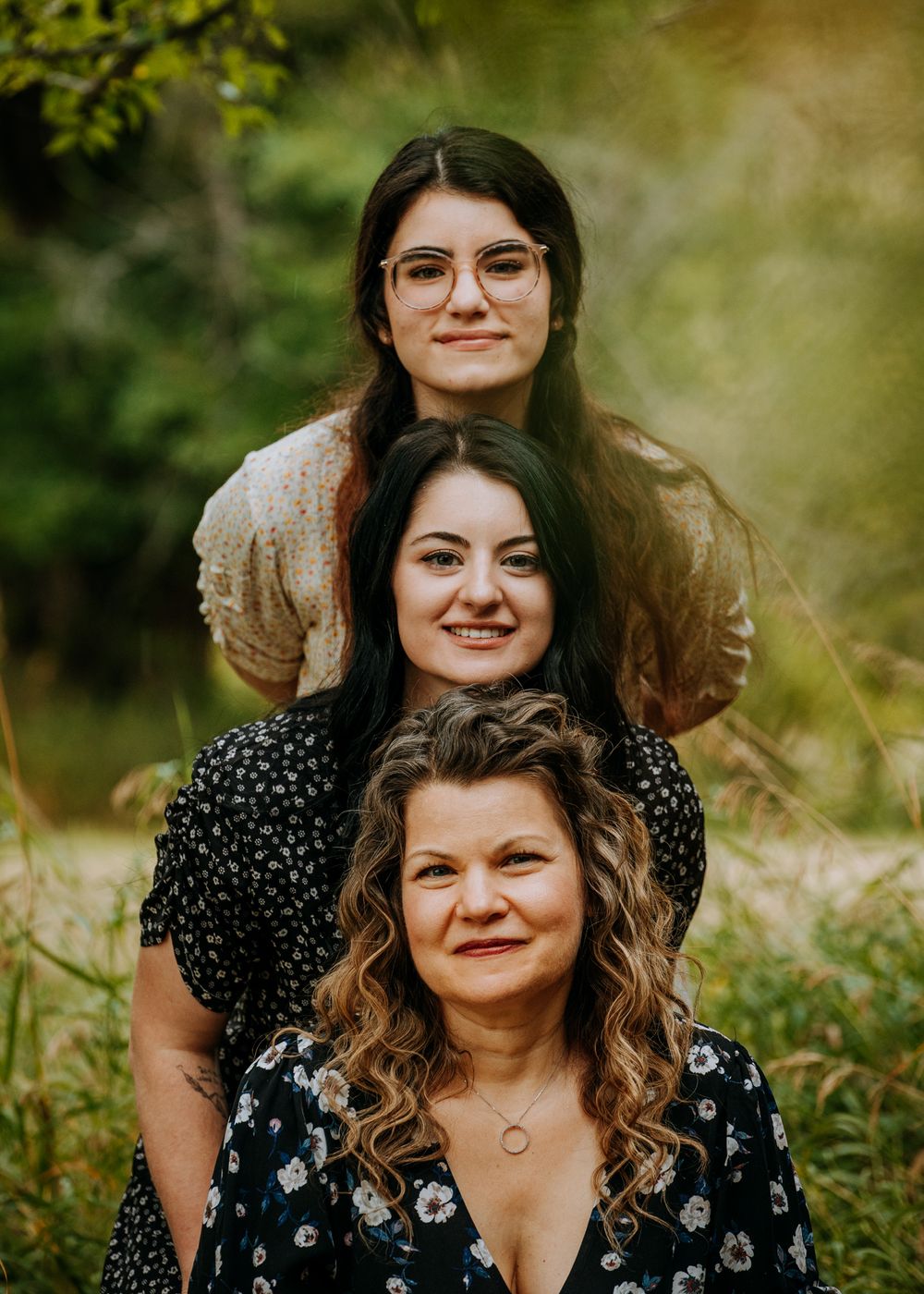 Three friends pose together in patterned dresses for a portrait in a natural outdoor setting.