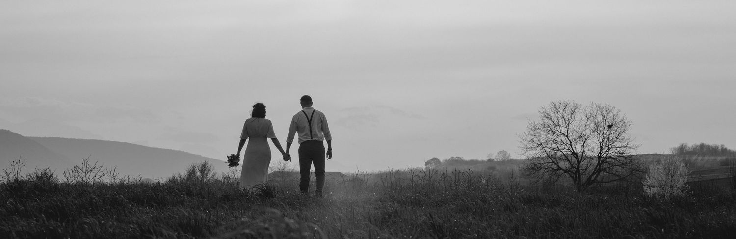 Black and white silhouette of couple walking hand in hand across a hilltop landscape.