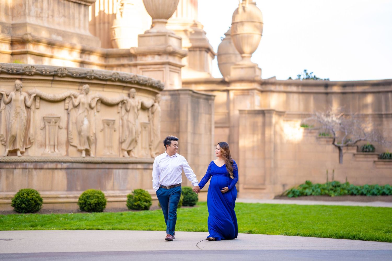 A couple walking together in formal attire near ornate architectural columns.